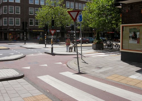 Ein Radweg führt um die Ecke, genau wie der Gehweg. Zebrastreifen für Fußgänger, den Radweg zu überqueren. Ampeln für den Fahrbahn zu zu Fuß überqueren oder mit Rad überfahren.